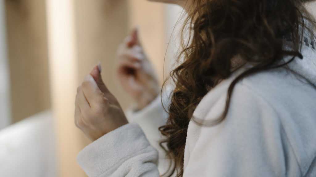 Jeune femme appliquant un soin du visage dans une salle de bain pour illustrer une routine beauté et bien-être